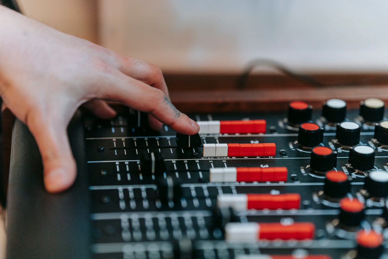 about-us Hand adjusting mixer controls in a sound studio, showcasing precision and audio engineering.